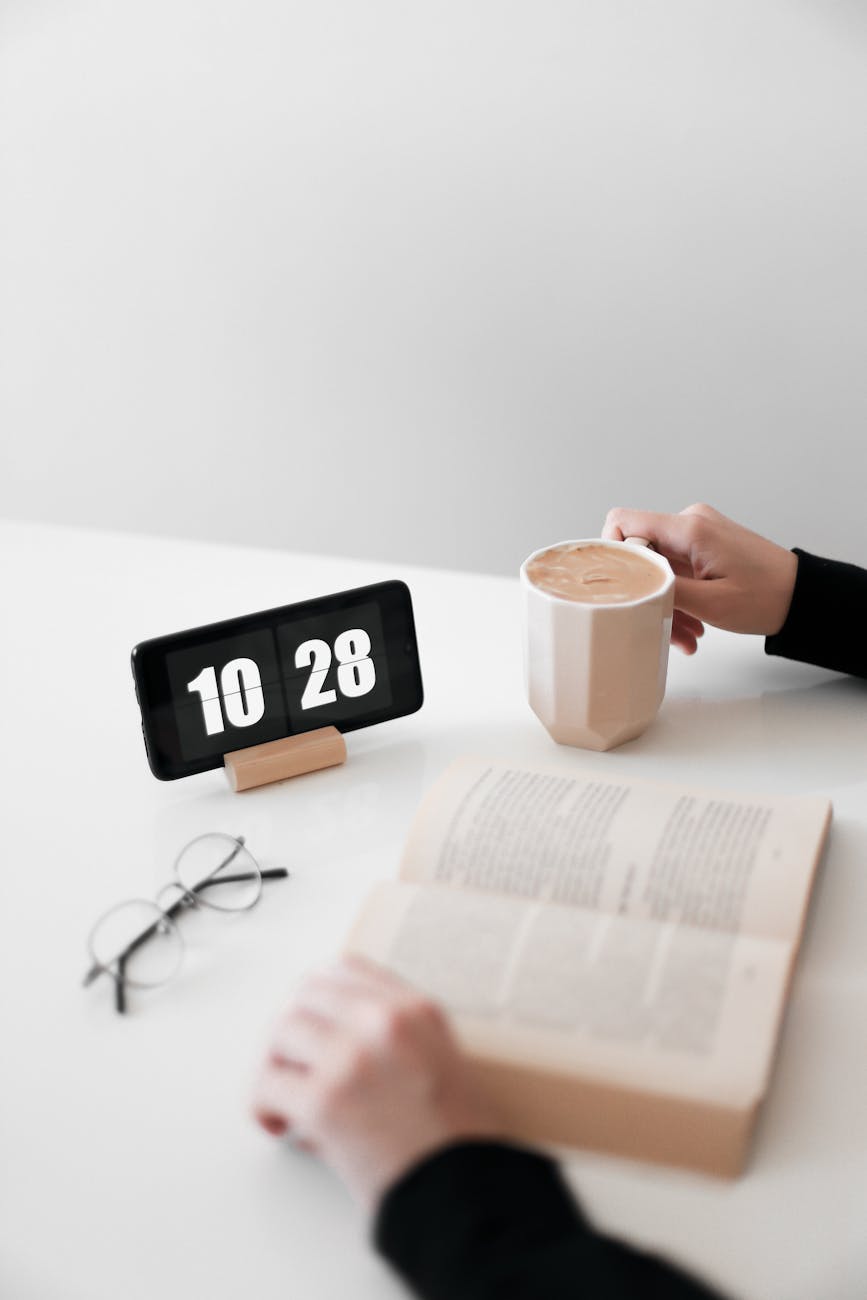 person reading a book with digital clock on a desk
